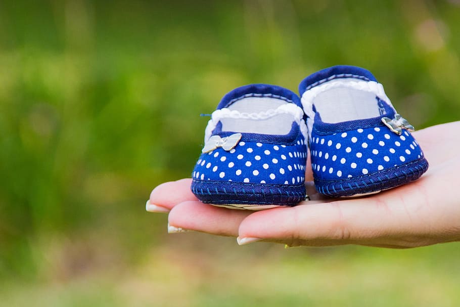 person holding girl's white-and-blue polka dot flat shoes, baby