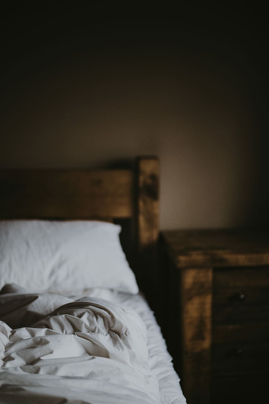 white cushion on bed near brown wooden nightstand, selective focus photography of white bed comforter