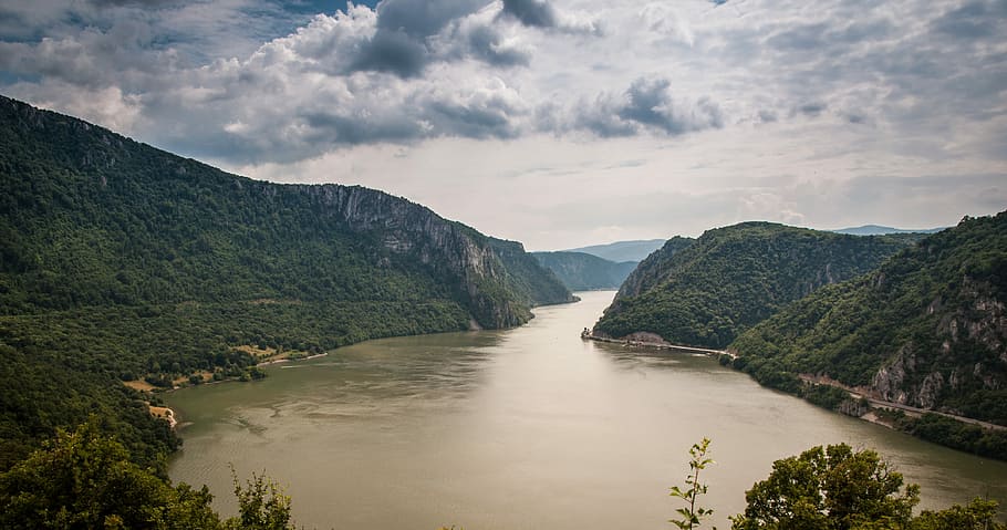 grey calm body of water between mountains and tall trees under white clouds at daytime, body of water surrounded by mountains covered with green leaf trees HD wallpaper