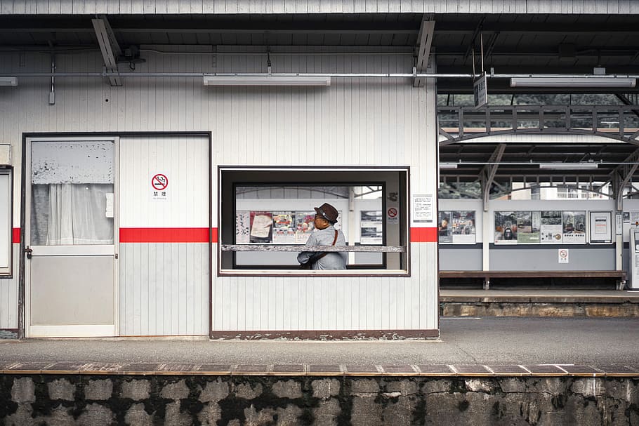 man wearing hat behind glass window, woman sitting on waiting shed in terminal HD wallpaper