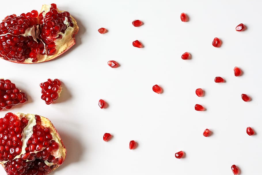 closeup photo of sliced pomegranate fruit, red fruits on white surface HD wallpaper