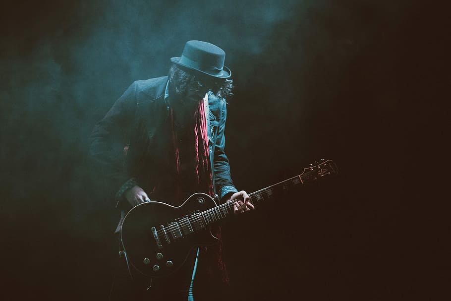 person wearing suit jacket and fedora hat playing guitar, music