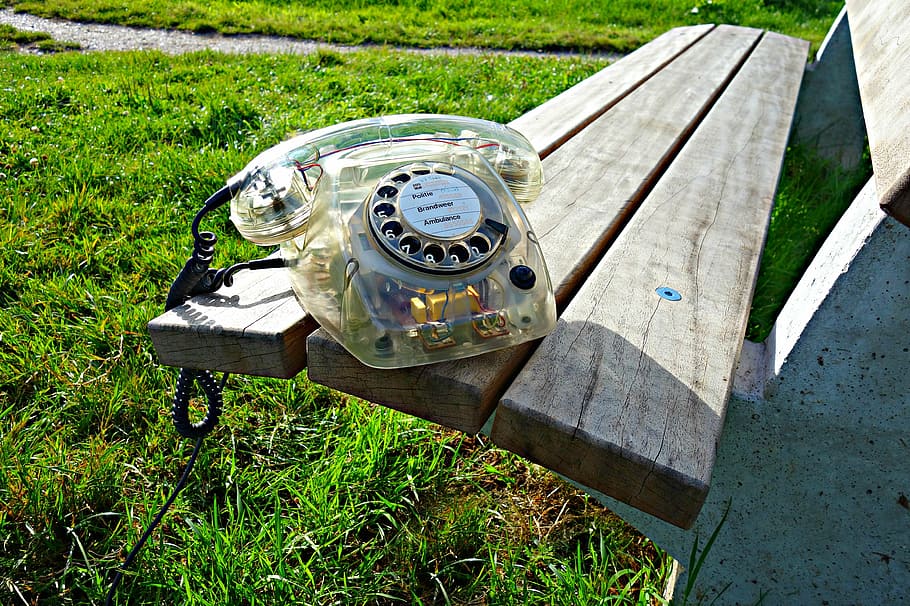clear rotary phone on wooden bench during daytime, telephone