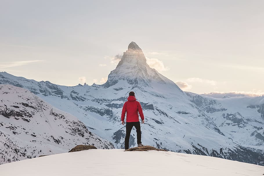 person in red hoodie standing on snowy mountain during daytime, person standing on mountain slope covered with snow