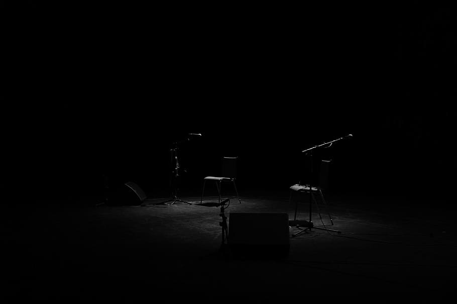 A dim shot of two chairs and microphone stands on an empty stage, untitled