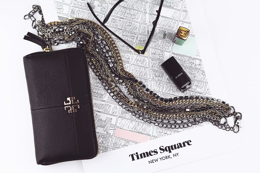 black sling bag, black Tory Burch leather long wallet with gold-and-silver chain necklace on table