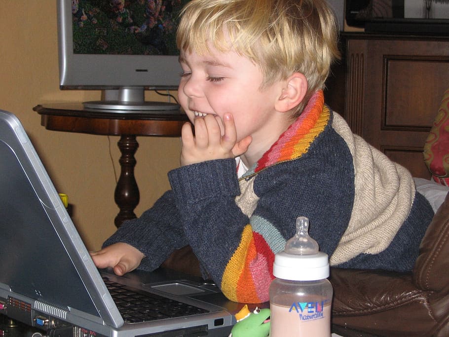 smiling blonde haired boy using laptop computer beside brown table HD wallpaper