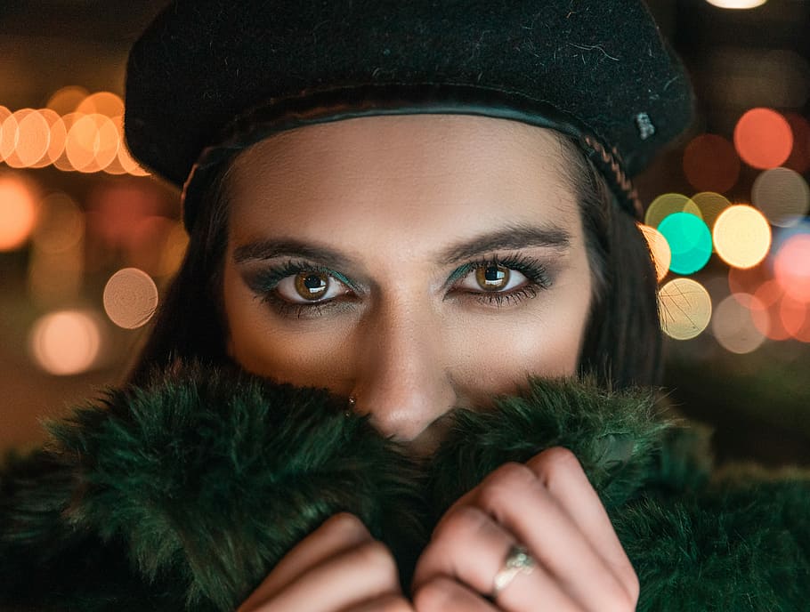 woman wearing green fur coat, bokeh photography of woman covering her face wearing black hat HD wallpaper
