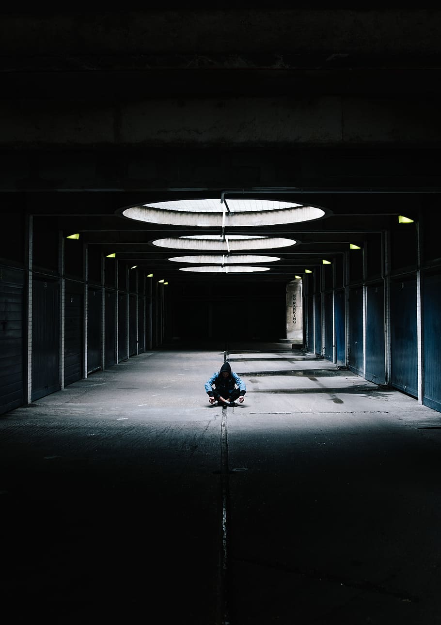person sitting cross leg at hallway under glass ceiling between black wall, man sitting on gray concrete floor inside room HD wallpaper