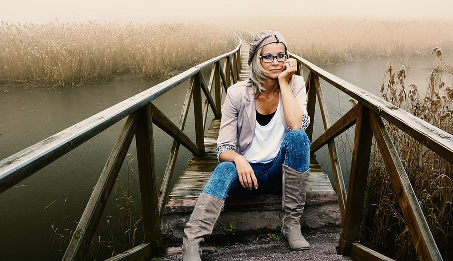 woman in white shirt with brown cardigan and brown boots sitting on brown wooden bridge during daytime HD wallpaper