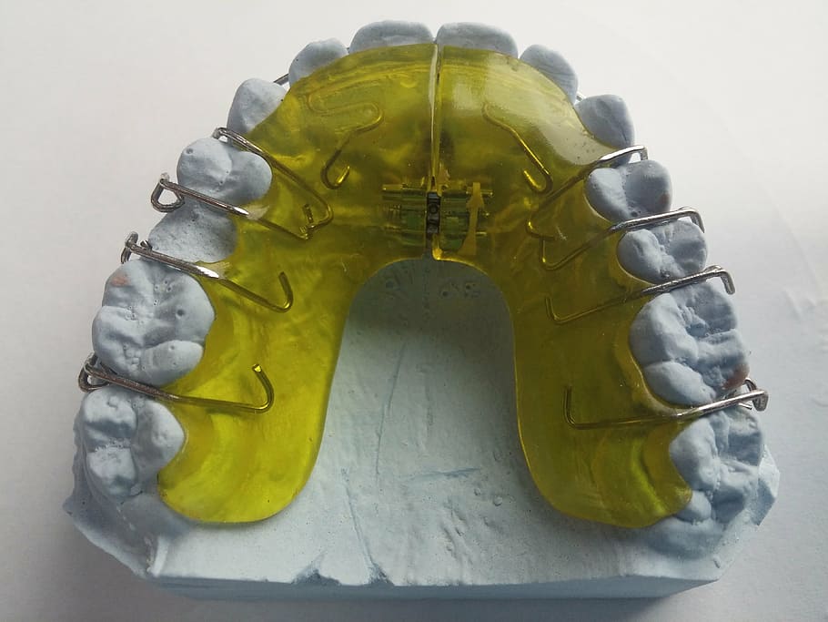 yellow and white teeth brace molder on white surface, dental braces