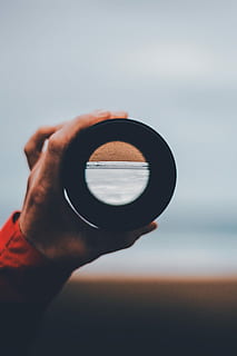 person holding black scope, lens, circle, hand, beach, upside down HD wallpaper