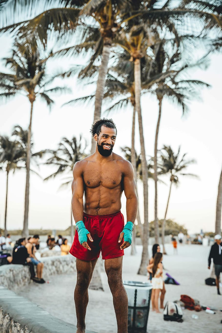 man wearing red shorts standing on concrete fence near coconut tree on seashore HD wallpaper