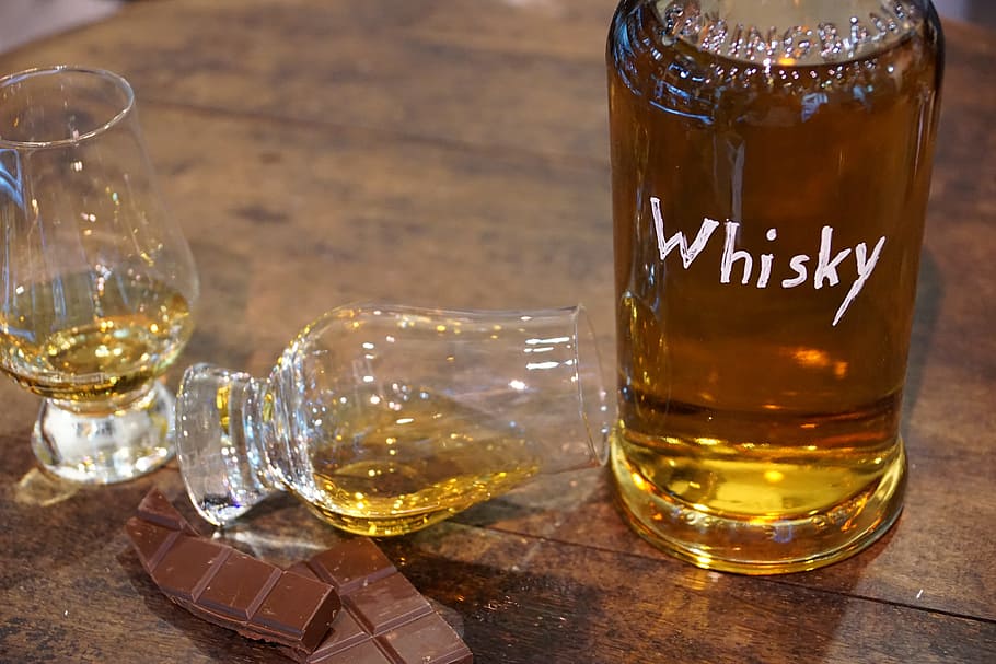 whisky bottle beside two clear drinking glasses and chocolate bar on brown wooden surface