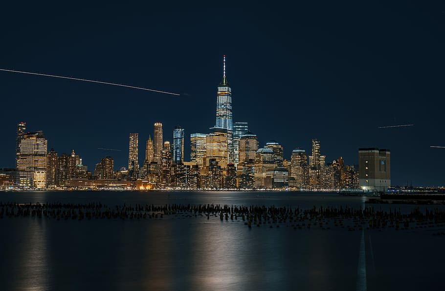 time lapse photography of skyscraper, cityscape photography of lighted buildings with rocks on body of water HD wallpaper