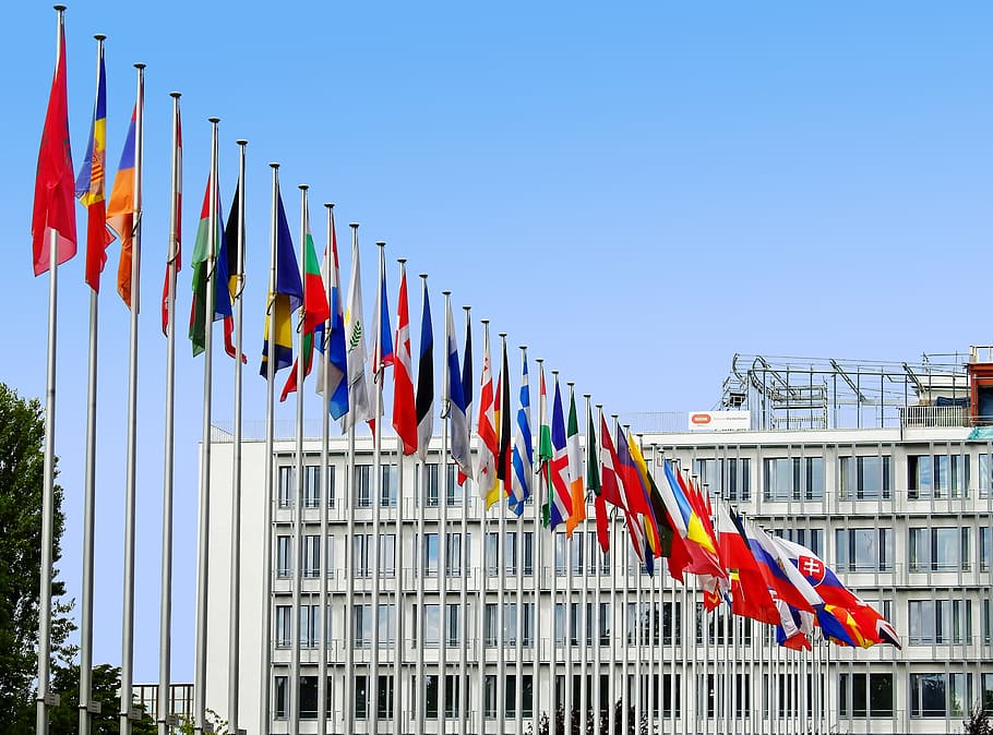 line of assorted-color flags beside white concrete building under blue sky at daytime HD wallpaper