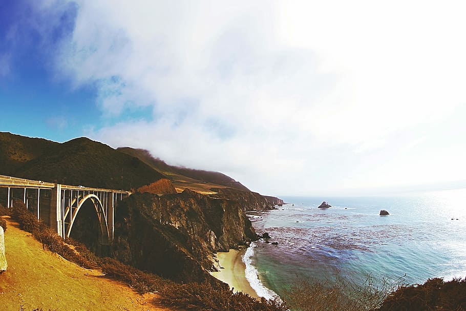 brown mountain near seawater under blue sky during daytime, brown cliff near sea with bridge HD wallpaper