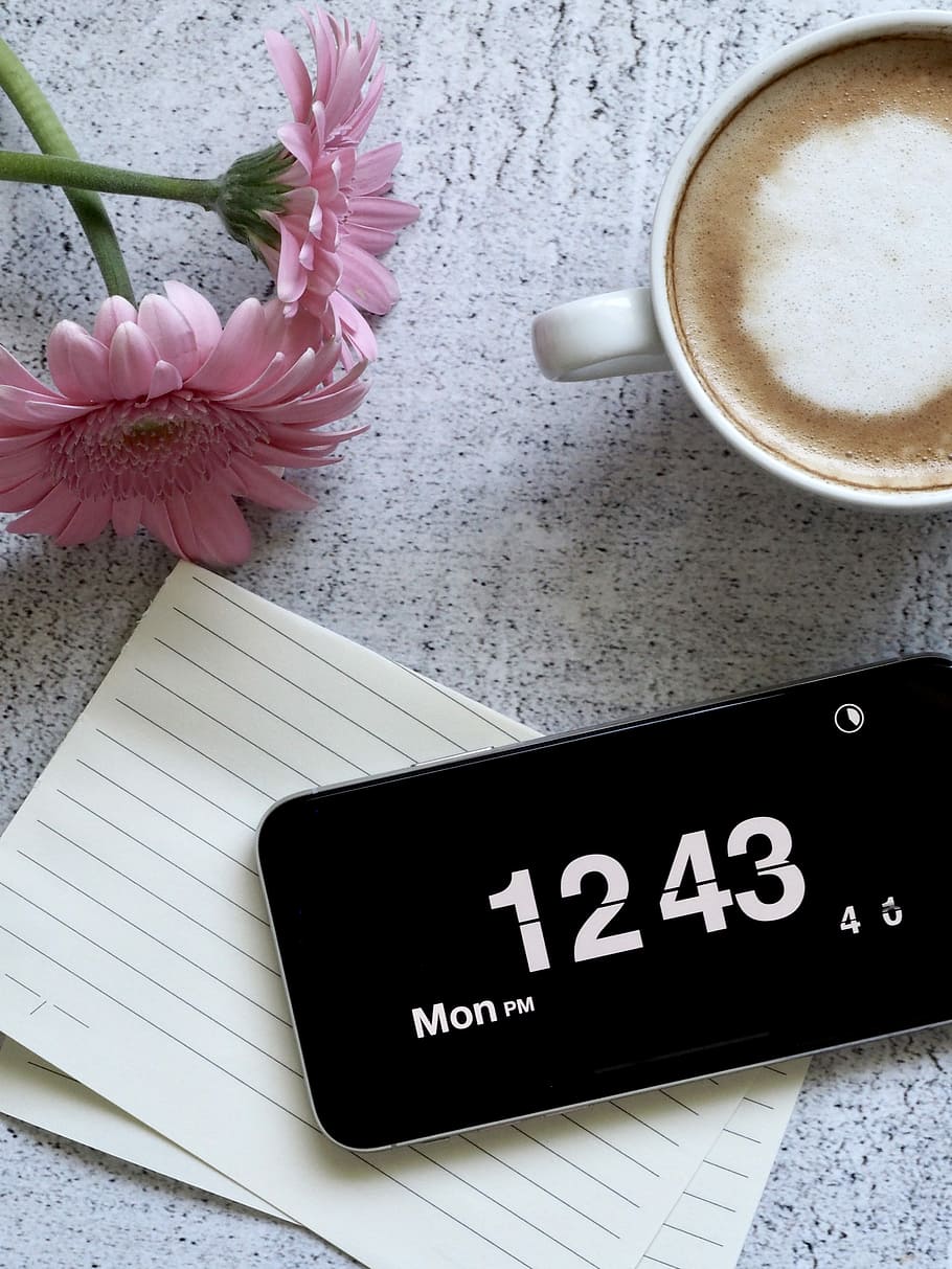 black smartphone displaying 12:43, a cup of coffee beside smartphone and pink flower HD wallpaper
