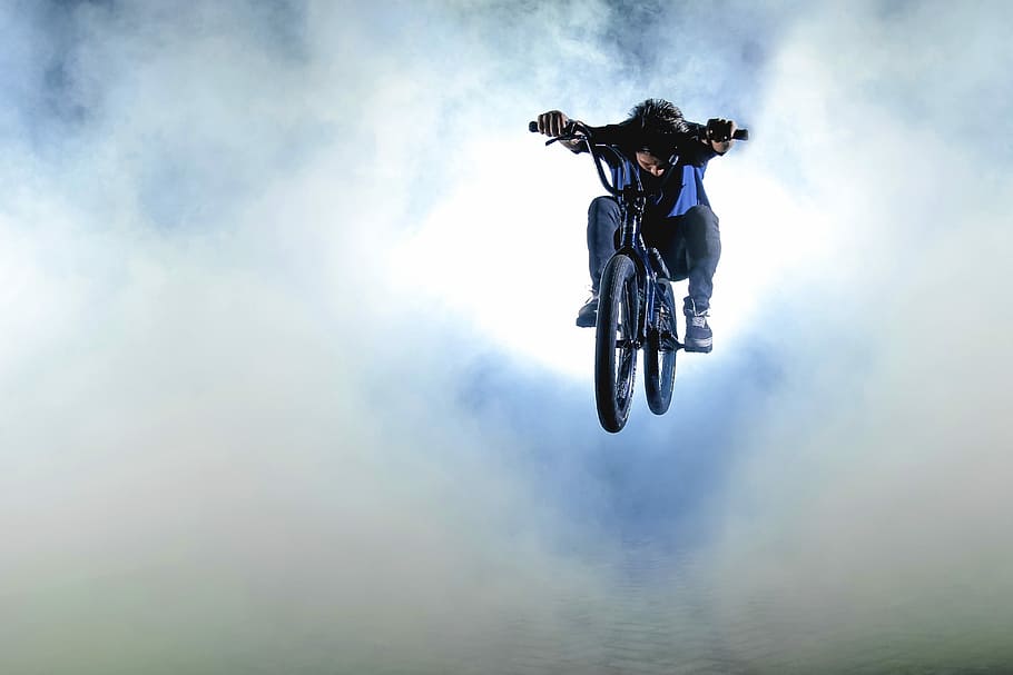 person riding on black bicycle, photography of man rides on bicycle with smokes