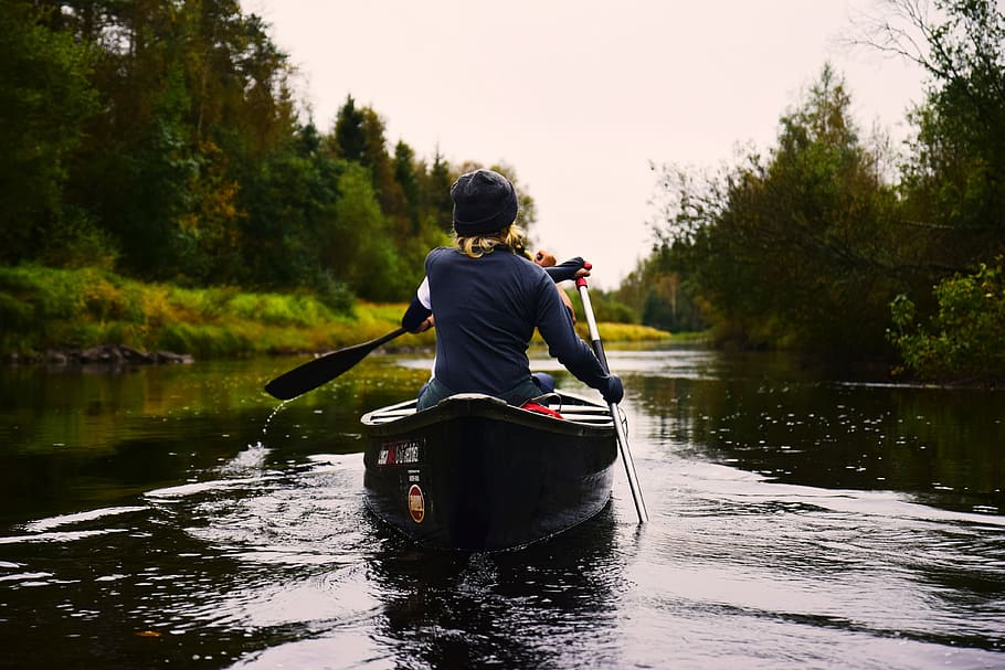 person in blue long-sleeved shirt sitting on kayak while paddling on body of water during daytime, person in black long-sleeve shirt riding black canoe during daytime