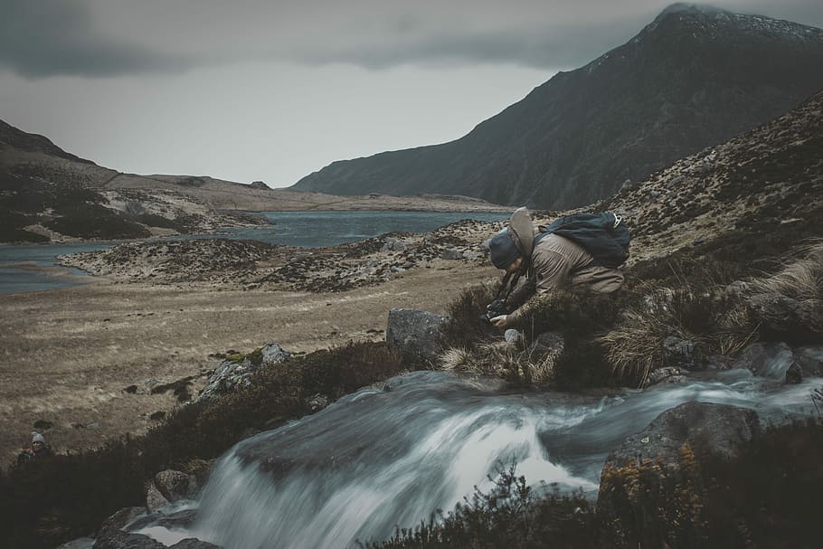 man on ground beside river during daytime, man taking photo of river HD wallpaper