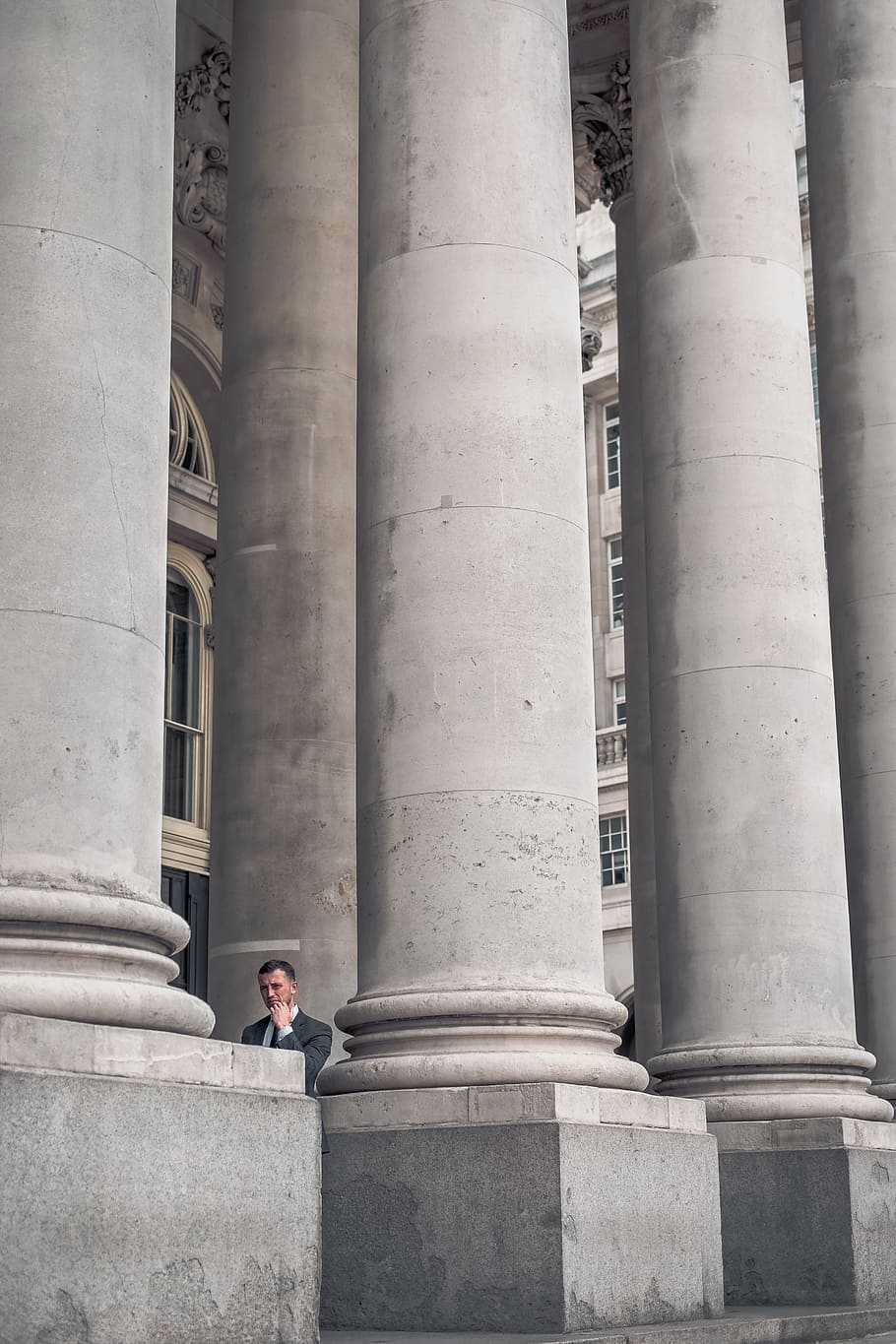 man standing beside gray concrete pillars, between the columns HD wallpaper