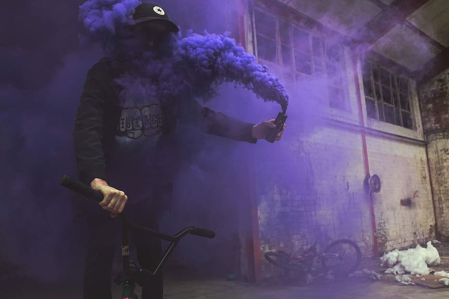 man riding bike, person riding BMX bike while holding black smoke bottle inside building