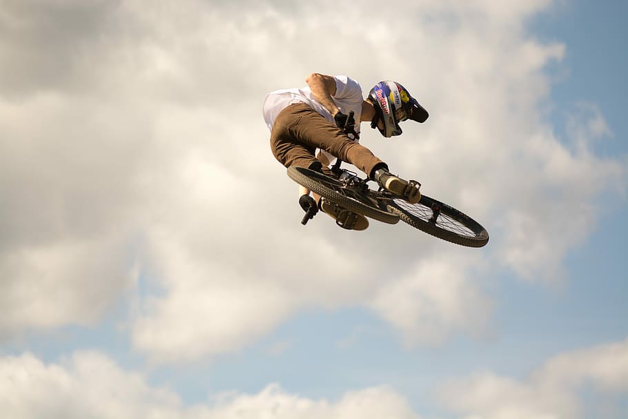 man doing BMX stunt, low angle photography of person wearing white shirt and helmet riding bicycle under white clouds during daytime, HD wallpaper