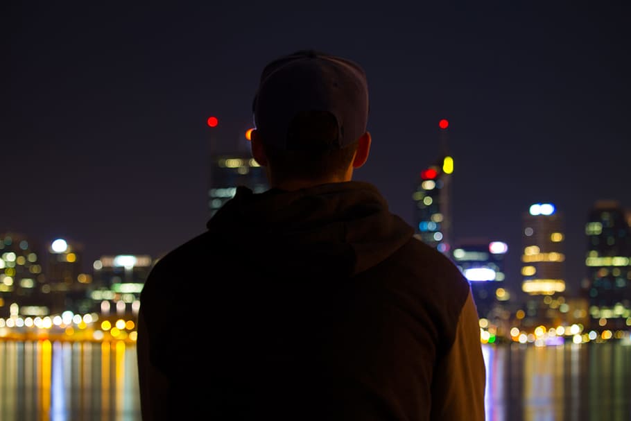 A man sitting at night looking at the city lights, people, men