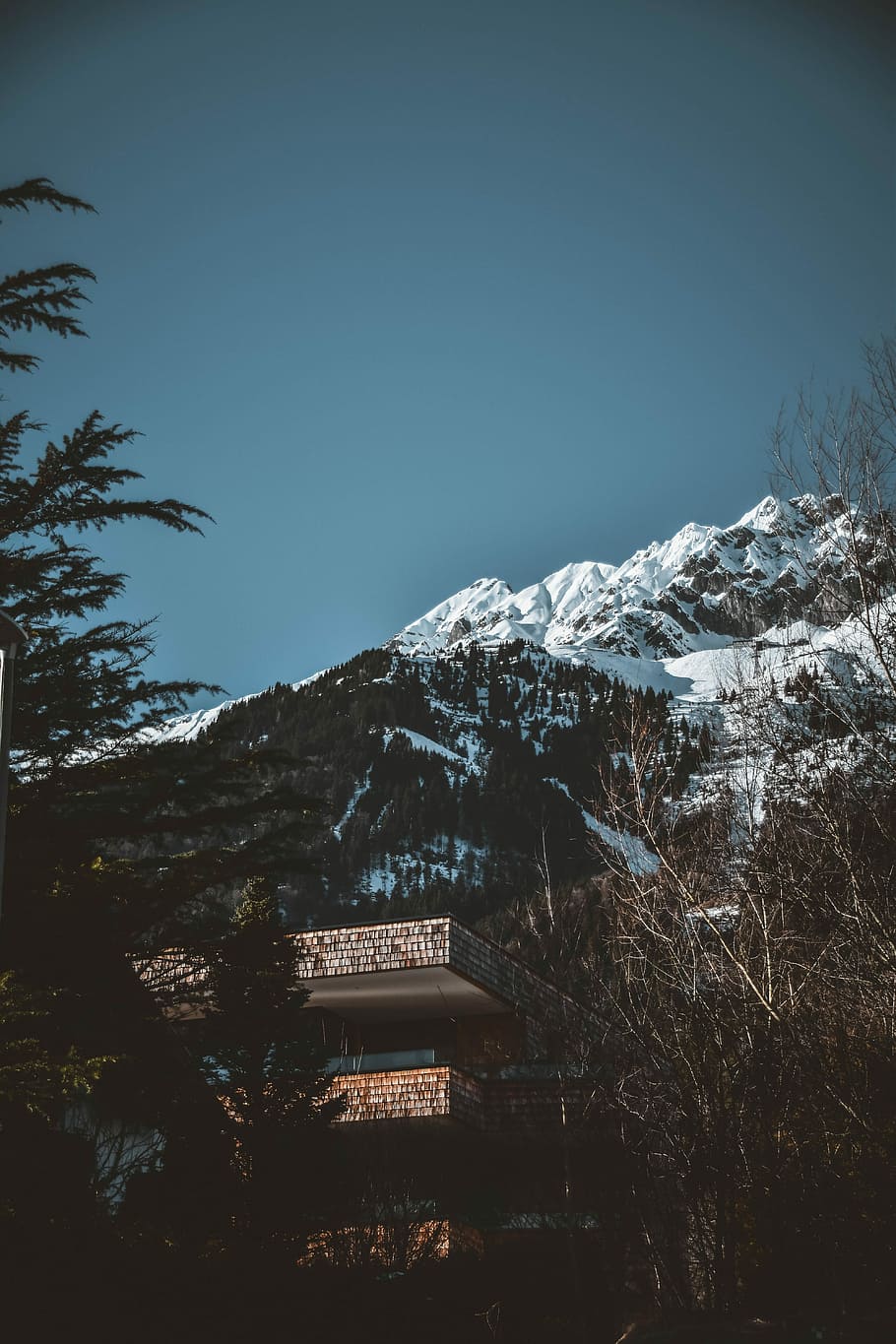brown concrete building near mountain covered with snows at daytime, low-angle photography of building on snow-covered mountain slope HD wallpaper