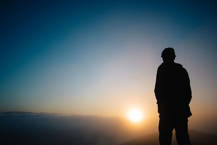 silhouette of a person during sunset, silhouette of man standing mountain facing sun