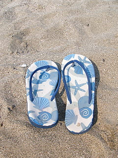 pair of white-and-blue starfish print flip-flops on gray sand HD wallpaper