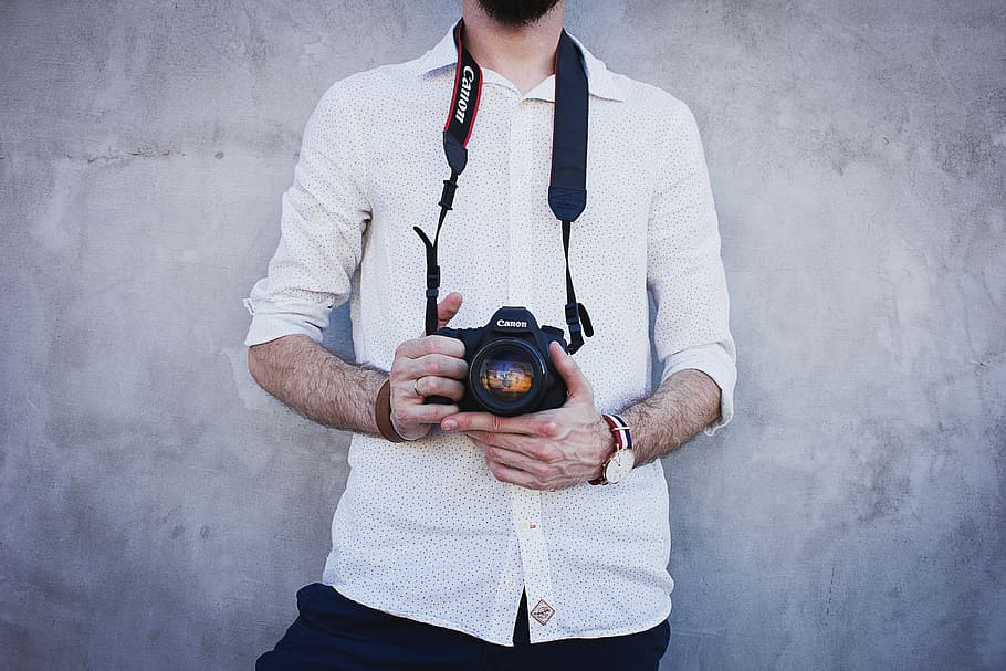 man in white dress shirt holding Canon DSLR camera, man holding camera leaning on wall HD wallpaper
