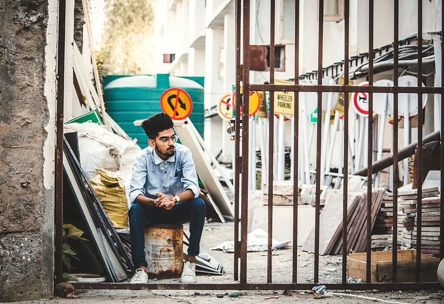 man sitting beside gate, man sitting on white can near open gate HD wallpaper