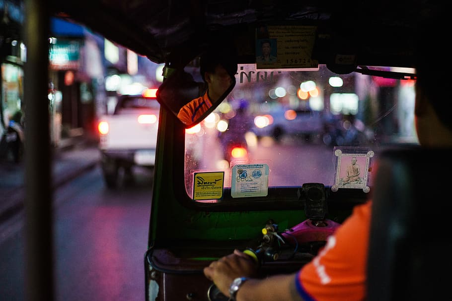 man sitting on vehicle, selective focus photography of man driving auto rickshaw at night