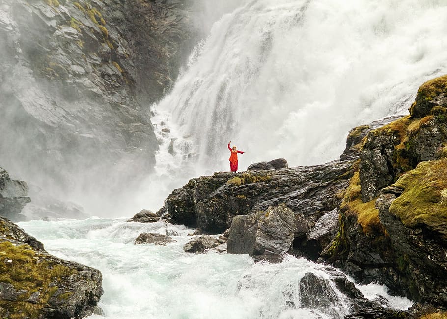 person standing on rock surrounded by waterfalls and river during daytime HD wallpaper