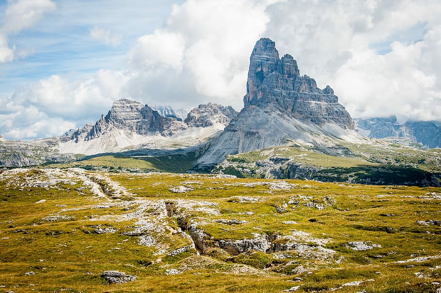 rock formation on wide field grass under cloudy blue sky during daytime, mountain across the land during daytime HD wallpaper