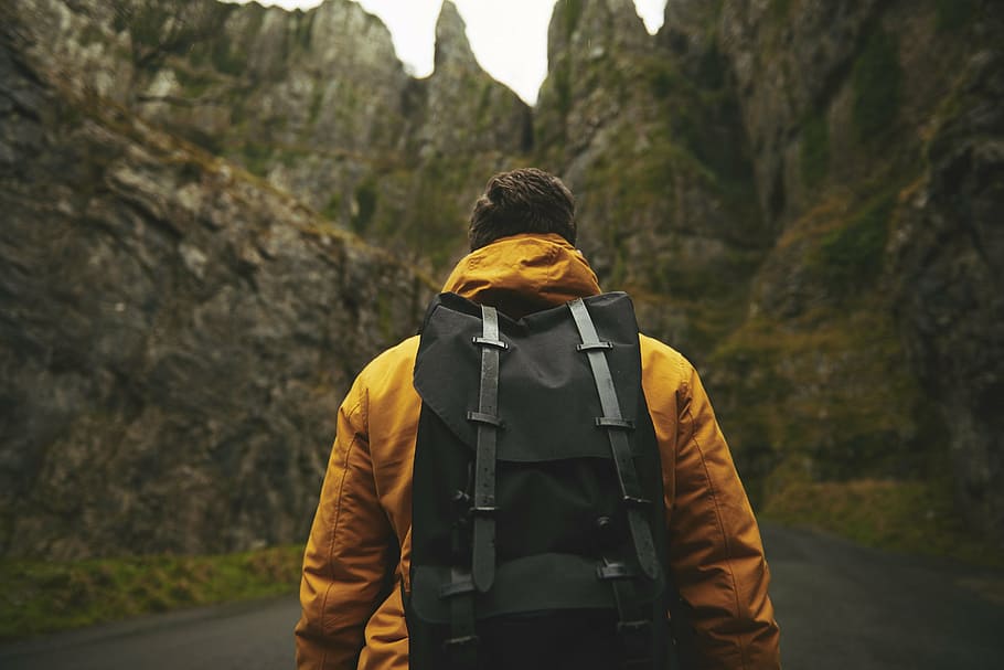 man wearing yellow hoodie and backpack standing in-front of a rocky mountain, HD wallpaper