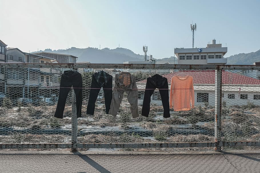 four assorted pants and orange shirt hanging on gray cyclone wire fence, four assorted-color pants hanging on gray cyclone fence during daytime HD wallpaper
