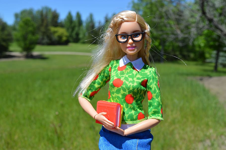 barbie doll action figure in front of green grass field, books