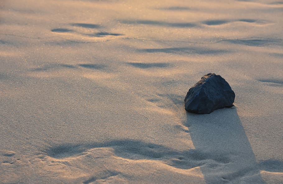 black stone fragment on white sand, closeup photo of black stone on sow ground HD wallpaper