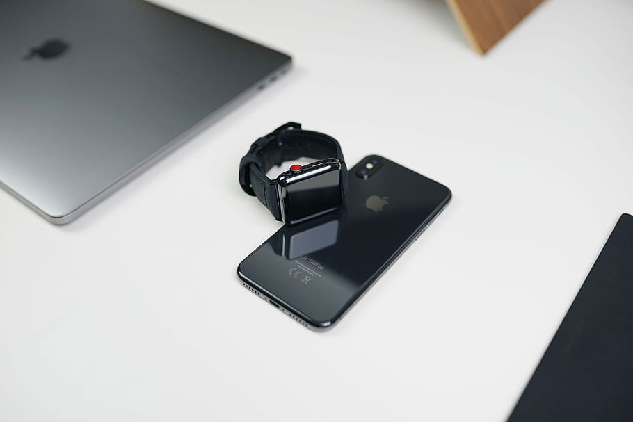 space gray aluminum case Apple Watch with black Sport Band on space gray iPhone X beside silver MacBook, space gray iPhone X and Apple Watch