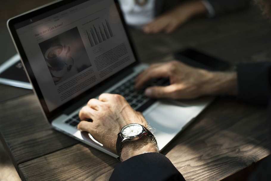 person wearing watch using silver laptop computer on brown table HD wallpaper