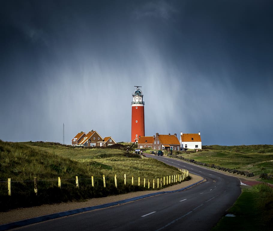 asphalt road between grass field going to brown lighthouse beside houses under cloudy sky, photo of roadway into lighthouse during daytime HD wallpaper