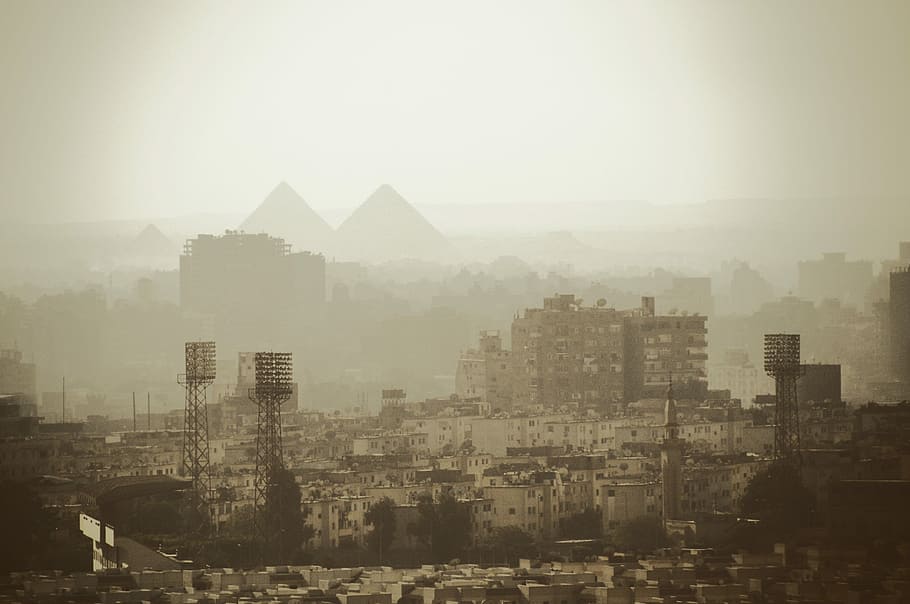 aerial photo of gray buildings near pyramids, city covered with fog during daytime HD wallpaper