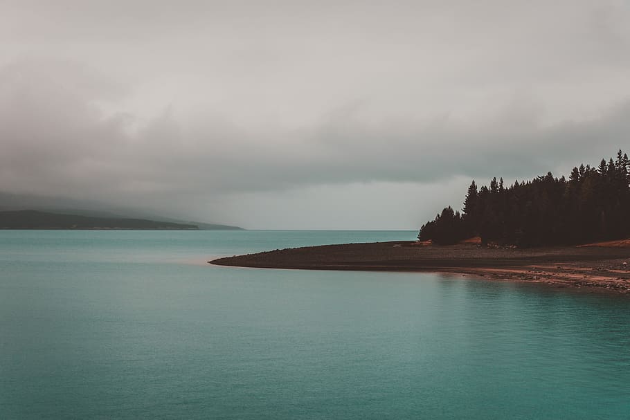 landscape photography of green beach under nimbus clouds, calm body of water near trees under white cloudy sky at daytime HD wallpaper