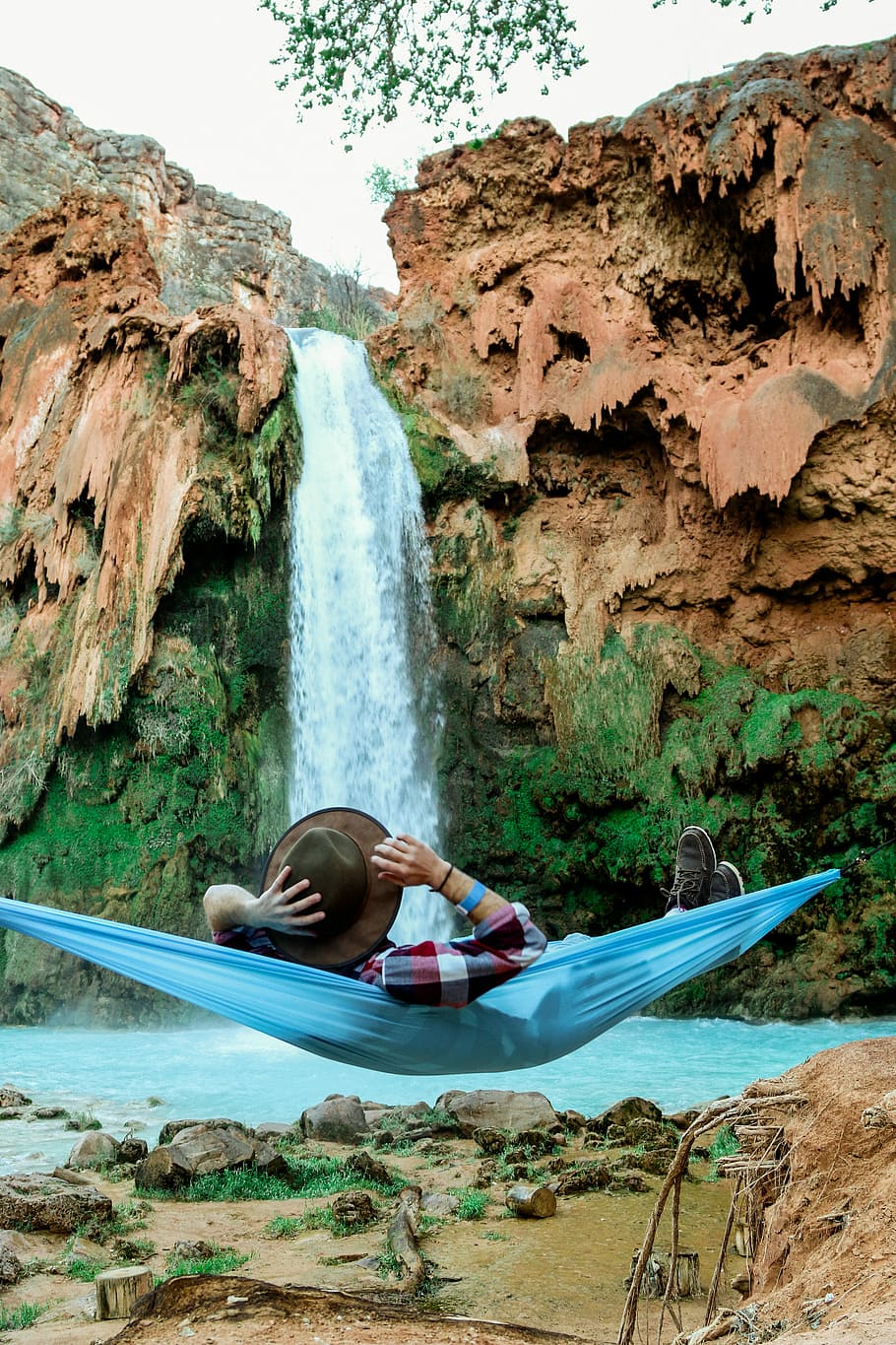 man laying on blue hammock in front of waterfalls, man in hammock in front waterfalls