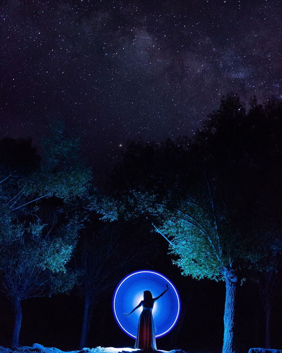 woman in dress standing in between trees, woman between tree during nighttime