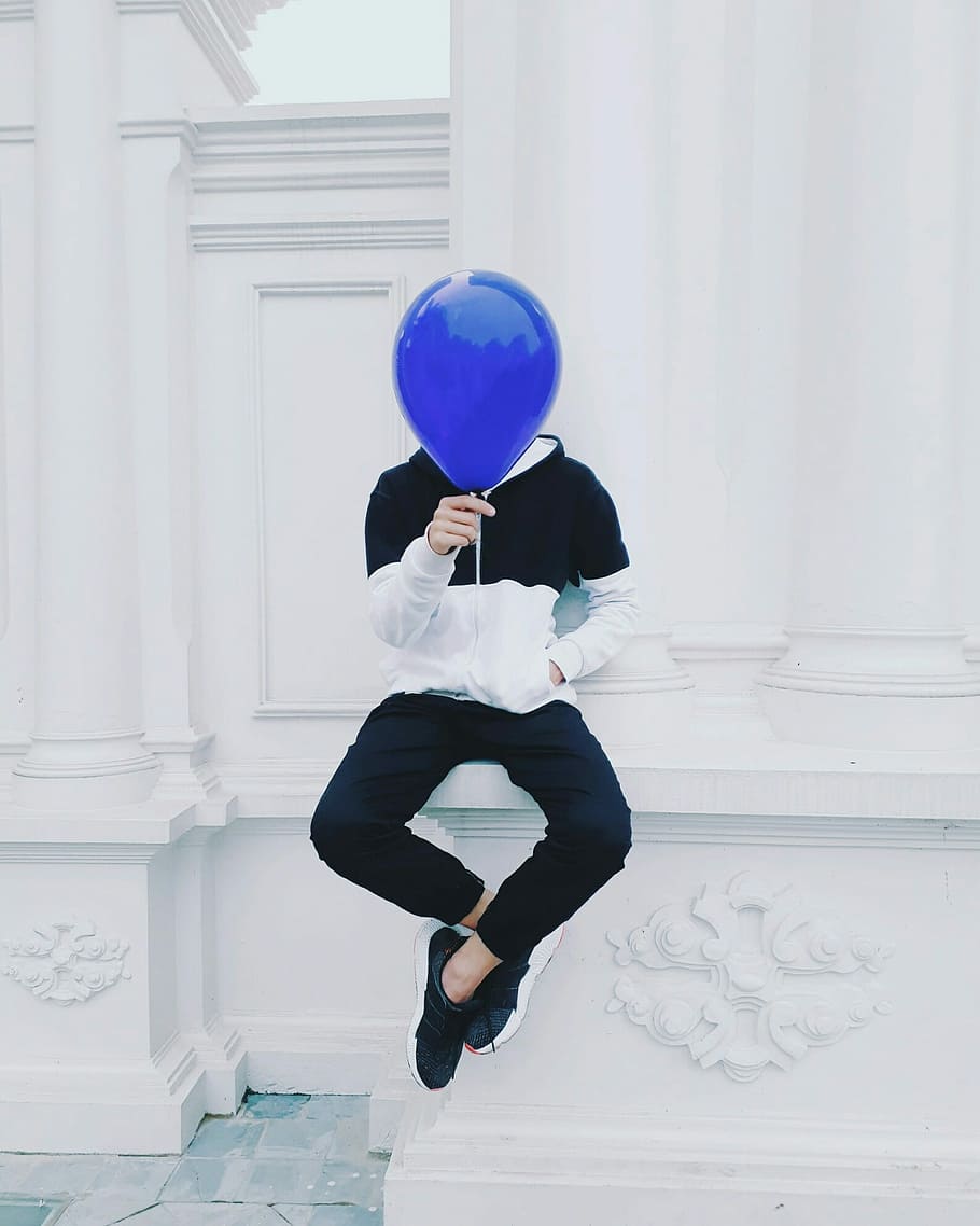 person sitting on white concrete pavement holding blue balloon at daytime, person in black and white full-zip hoodie while holding blue balloon HD wallpaper