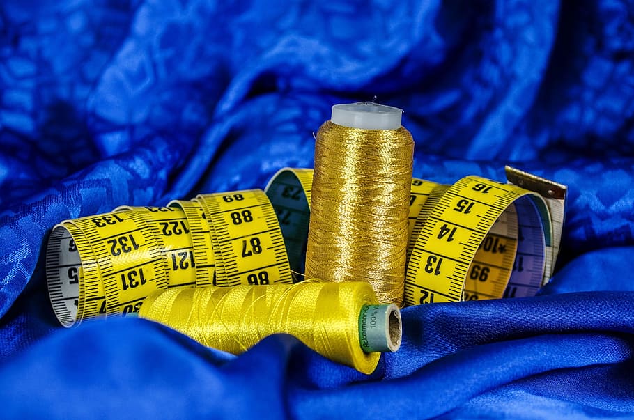 yellow tape measures and spools of thread on blue textile, sewing